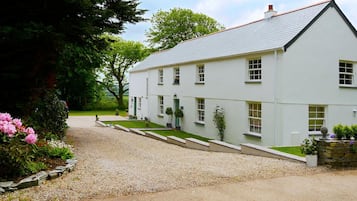Un bâtiment blanc à deux étages, avec une allée gravillonnée et un jardin bien entretenu.