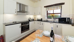 Una cocina moderna con armarios blancos, una mesa de madera y una ventana con vistas a zonas verdes.