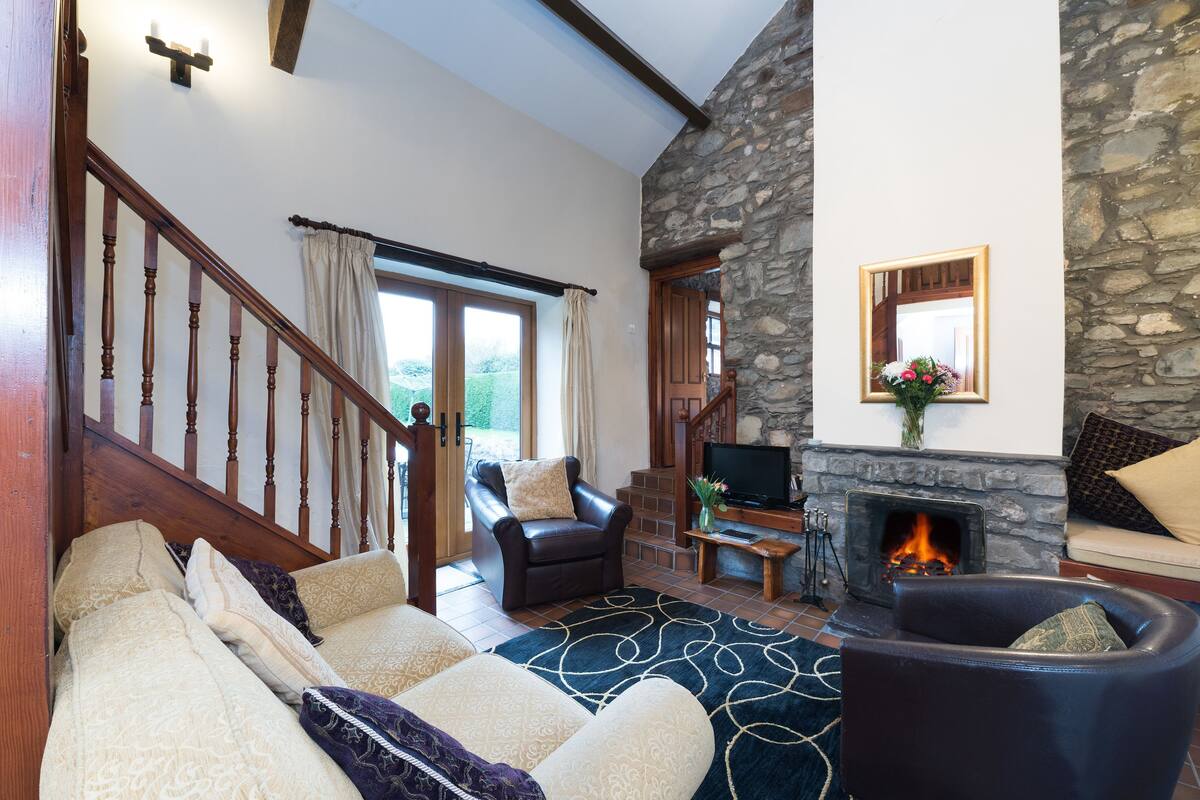 A living room with a stone fireplace, a wooden staircase, and a cozy seating area with sofas and a fire.