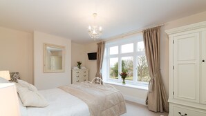Un dormitorio con cama, cómoda, espejo, ventana con cortinas y candelabro.