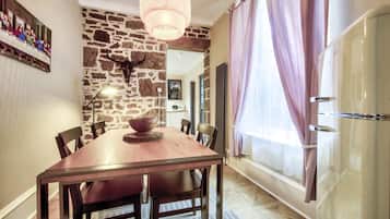 Un comedor con mesa de madera, sillas, pared de piedra, candelabro y refrigerador.