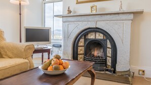 Una sala de estar con chimenea, un frutero sobre una mesa, un sofá y un televisor.