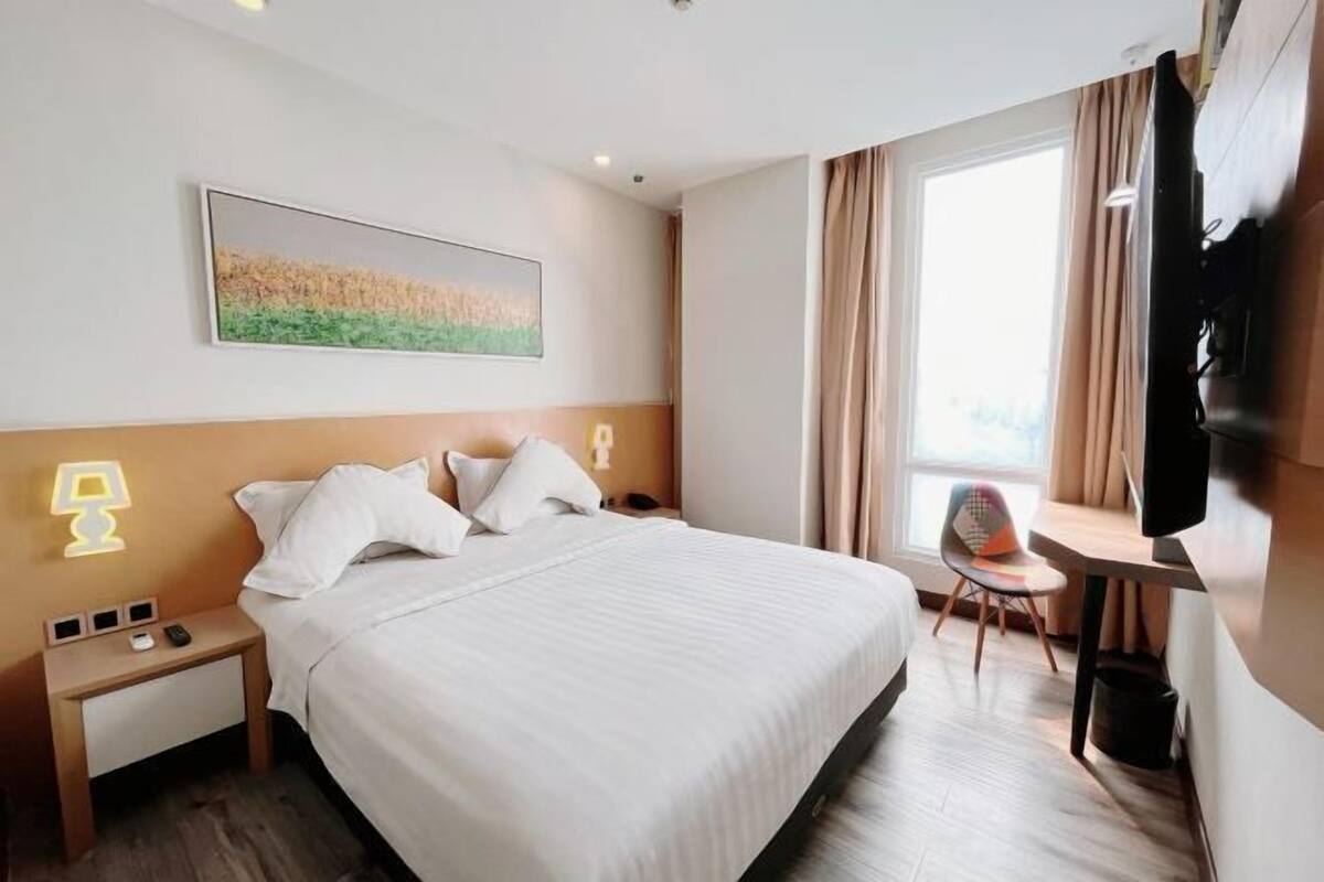 A hotel room with a bed, bedside tables, a desk with a chair, a television, and a window with curtains.