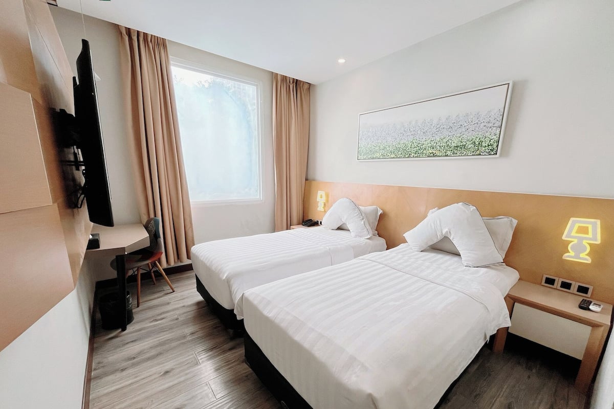 A hotel room with two beds, a desk, a TV, and a window with curtains.