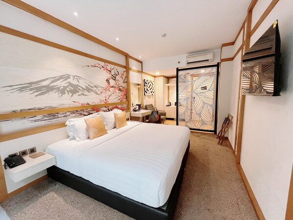 A hotel room with a large bed, a desk, a chair, a TV, and a wall with a mountain painting.