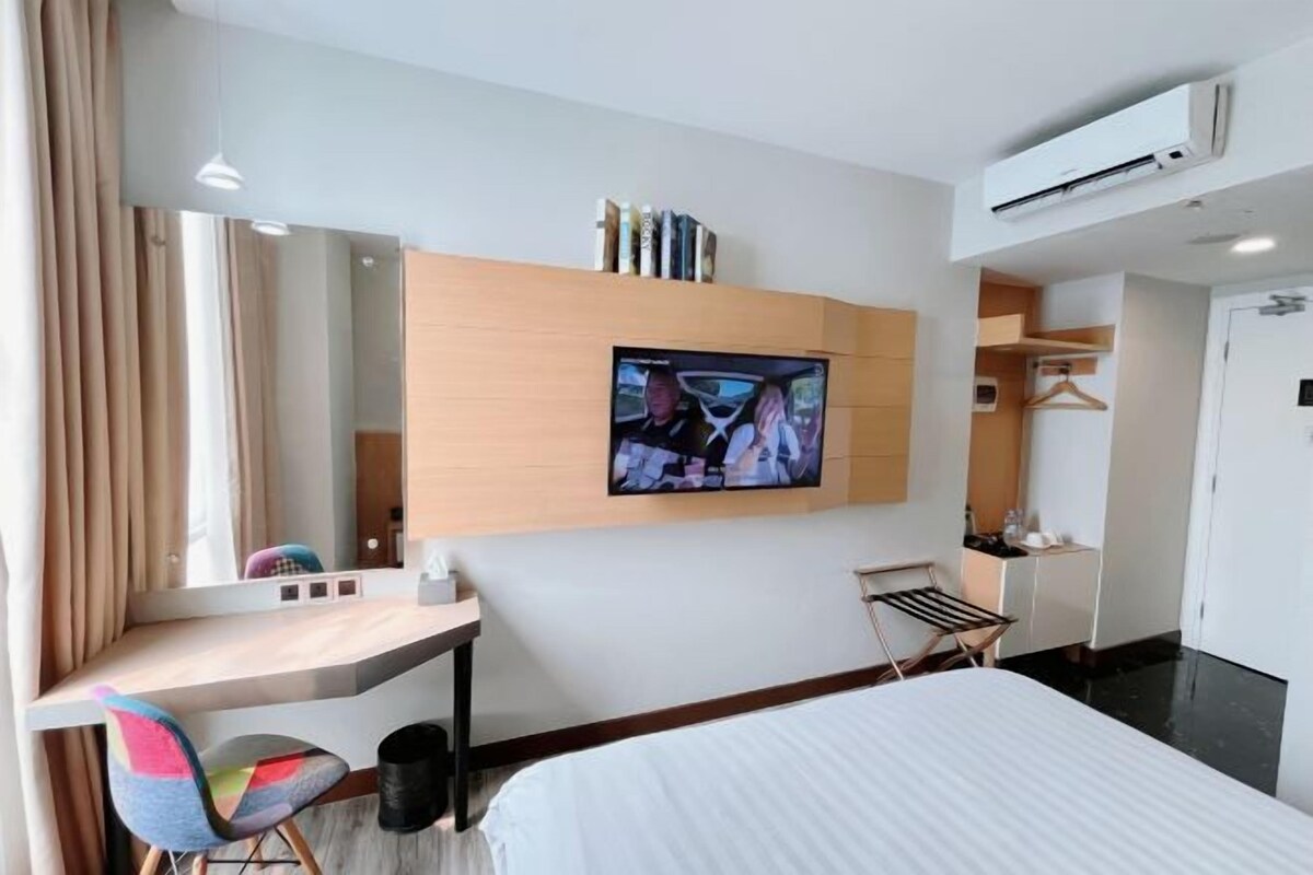A hotel room with a bed, a desk with a chair, a TV mounted on the wall, and a wardrobe.
