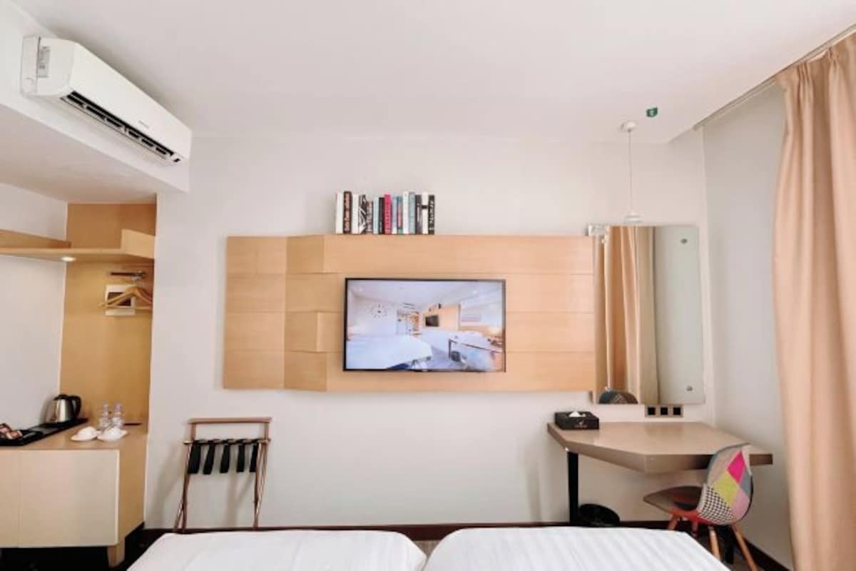 A hotel room with a bed, a desk, a chair, a TV mounted on the wall, and a coat rack.