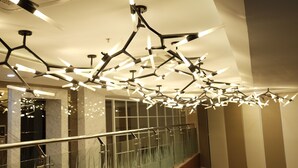 Un intérieur moderne agrémenté d’un luminaire au plafond aux formes géométriques originales et d’une rampe d’escalier en verre.