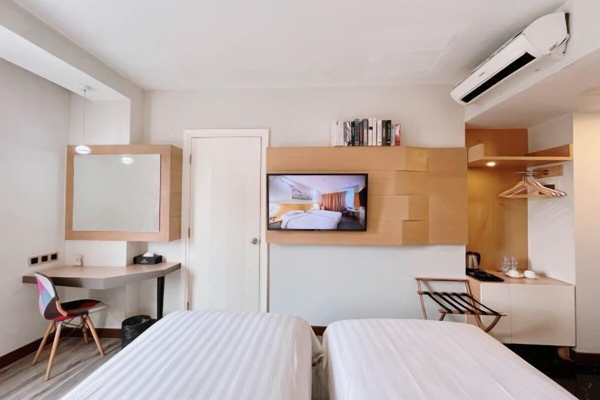 A hotel room with two beds, a desk with a chair, a television, a wardrobe, and a hanging clothes rack.