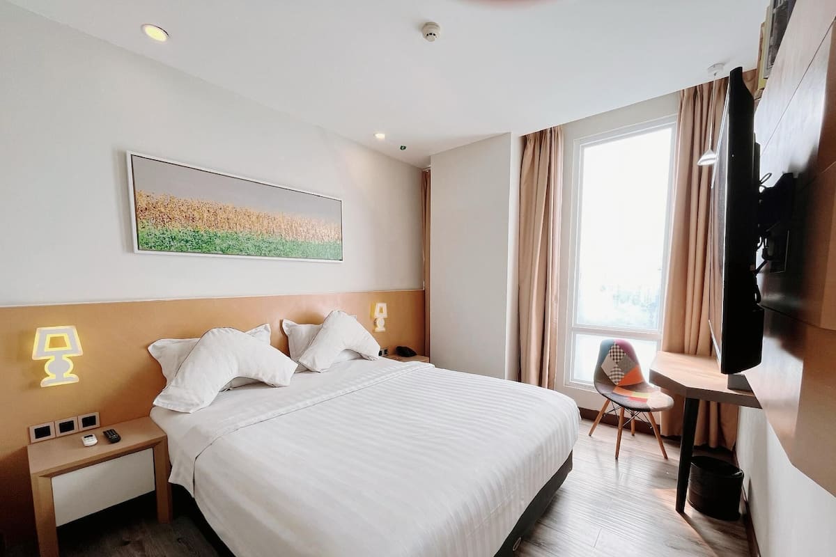 A hotel room with a large bed, bedside tables, a desk with a chair, a television, and a window with curtains.
