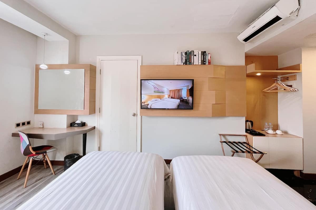 A hotel room with two beds, a desk, a TV mounted on the wall, and a wardrobe.