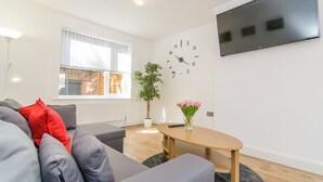 Una sala de estar moderna con un sofá gris, una mesa de centro de madera, una planta en maceta y un televisor instalado en la pared.