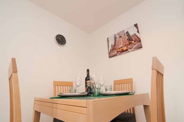 A dining area with a wooden table set for two, a clock, and a cityscape painting on the wall. - Warren House (Doncaster)