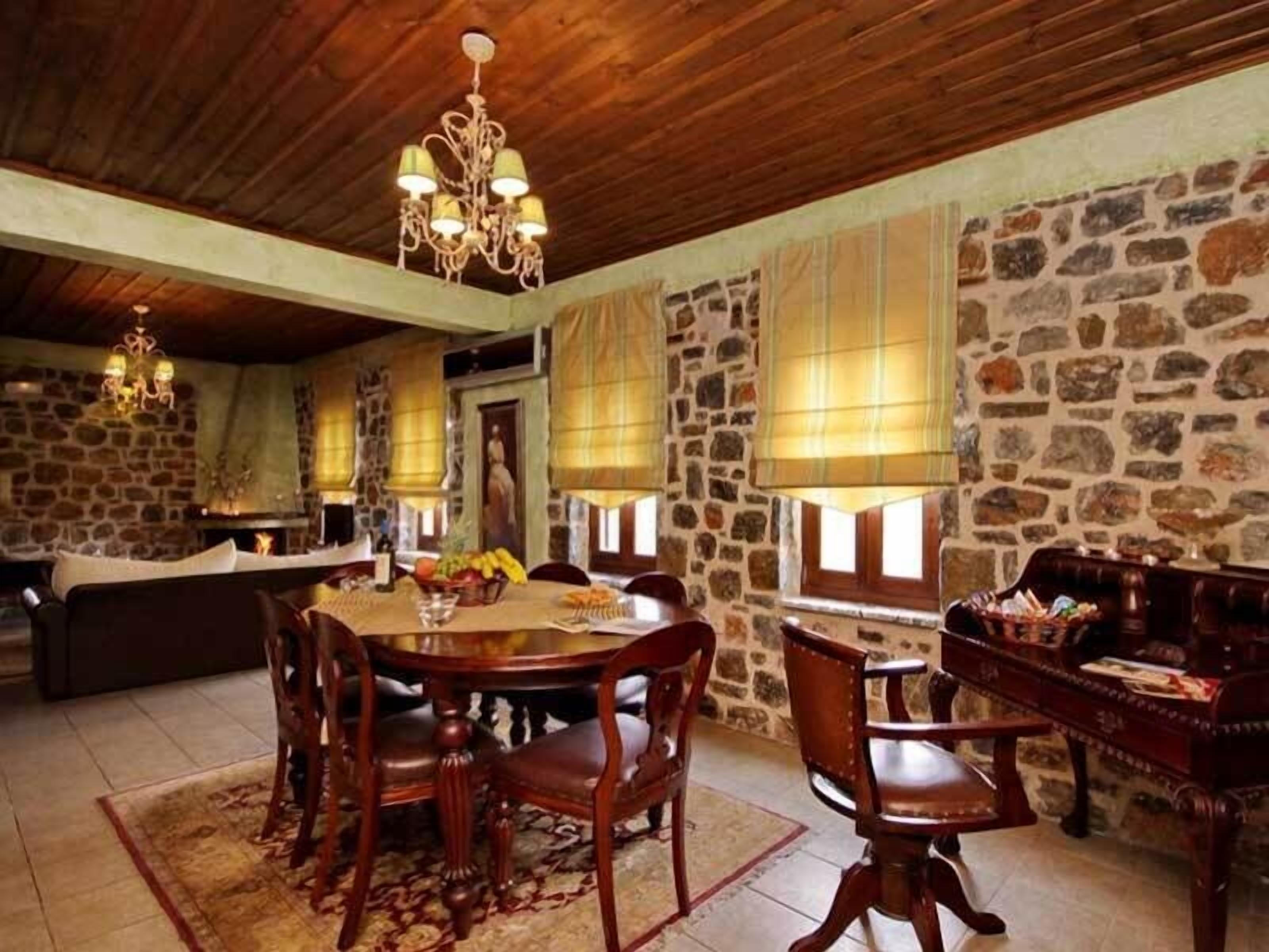 A rustic dining area with a stone wall, wooden ceiling, and a chandelier.
