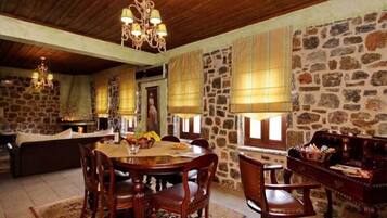 A rustic dining area with a stone wall, wooden ceiling, and a chandelier.