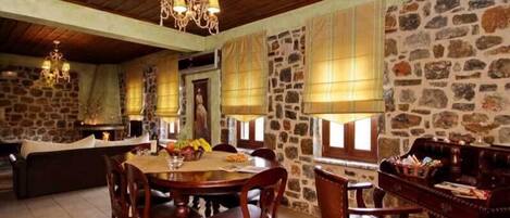A rustic dining area with a stone wall, wooden ceiling, and a chandelier.
