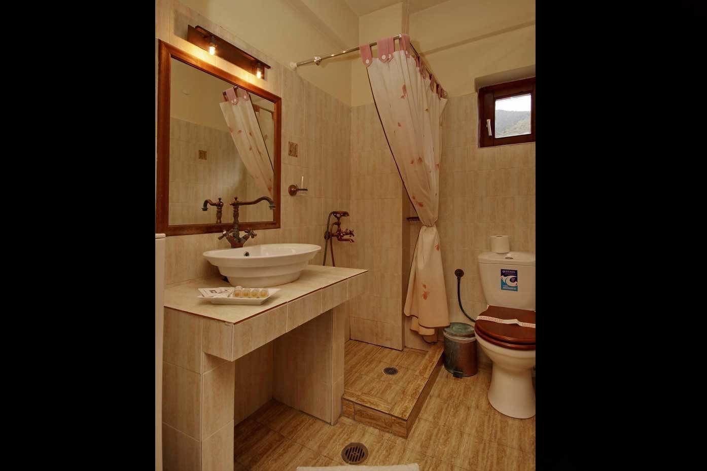A bathroom with a sink, mirror, shower curtain, toilet, and a window.