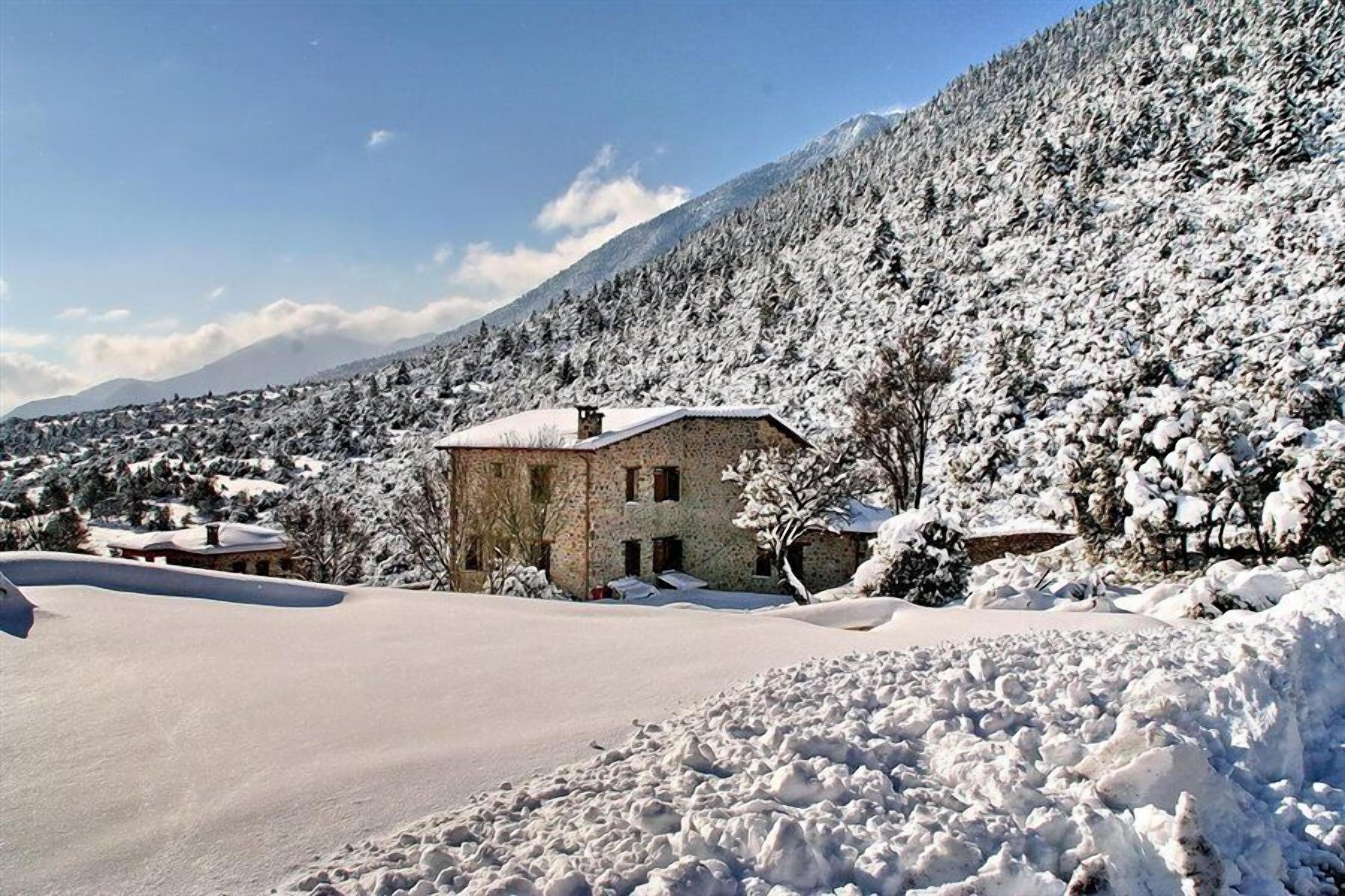 Un edificio de piedra con techo nevado, rodeado por un paisaje nevado y una montaña boscosa.