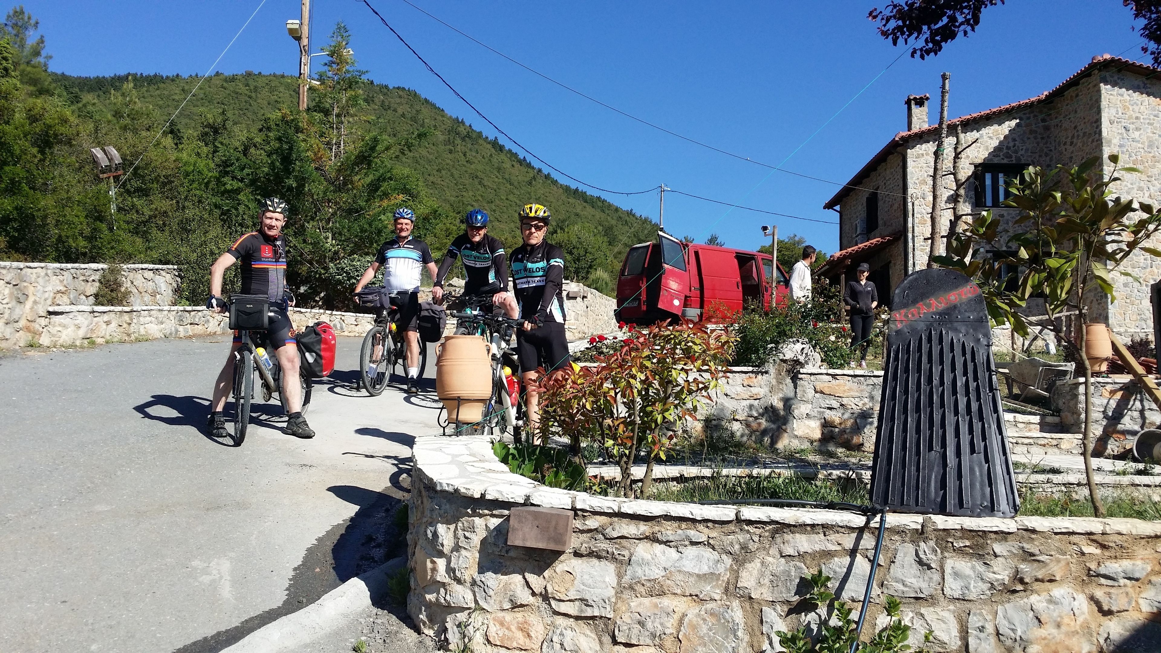 A group of cyclists on a road with a stone wall and a red vehicle parked nearby.