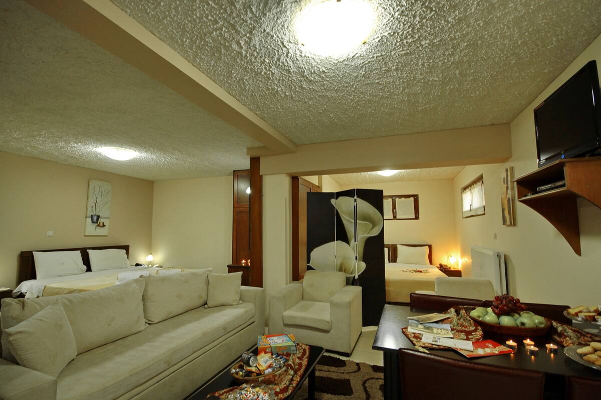 A hotel room with a sofa, armchair, dining table, and a TV.