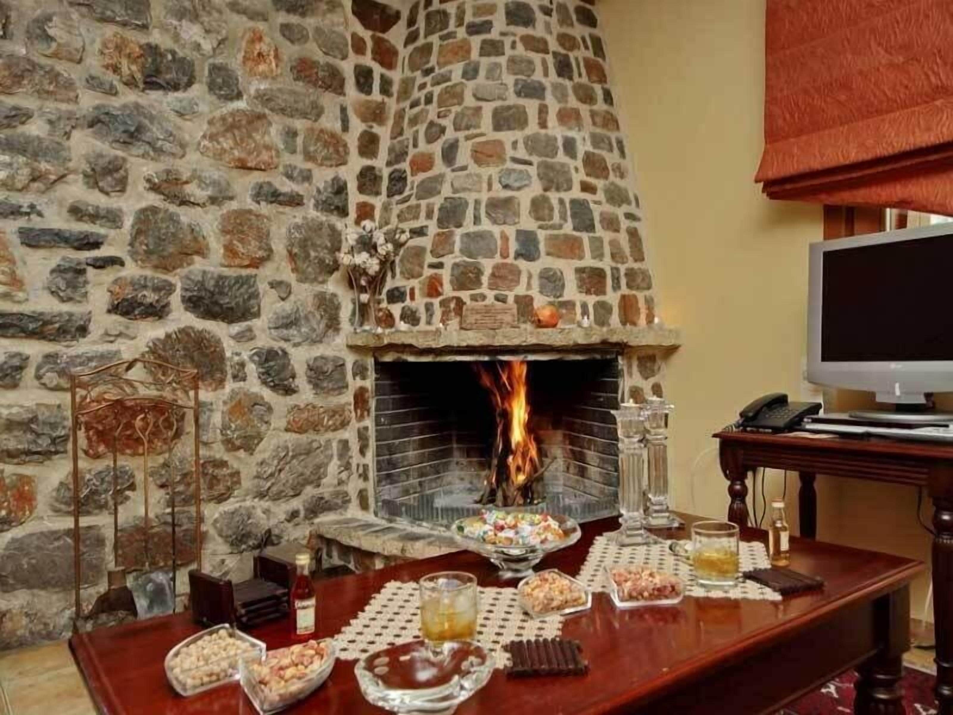 Una chimenea de piedra con fuego, una mesa de madera con aperitivos y bebidas, y un televisor sobre un mueble.