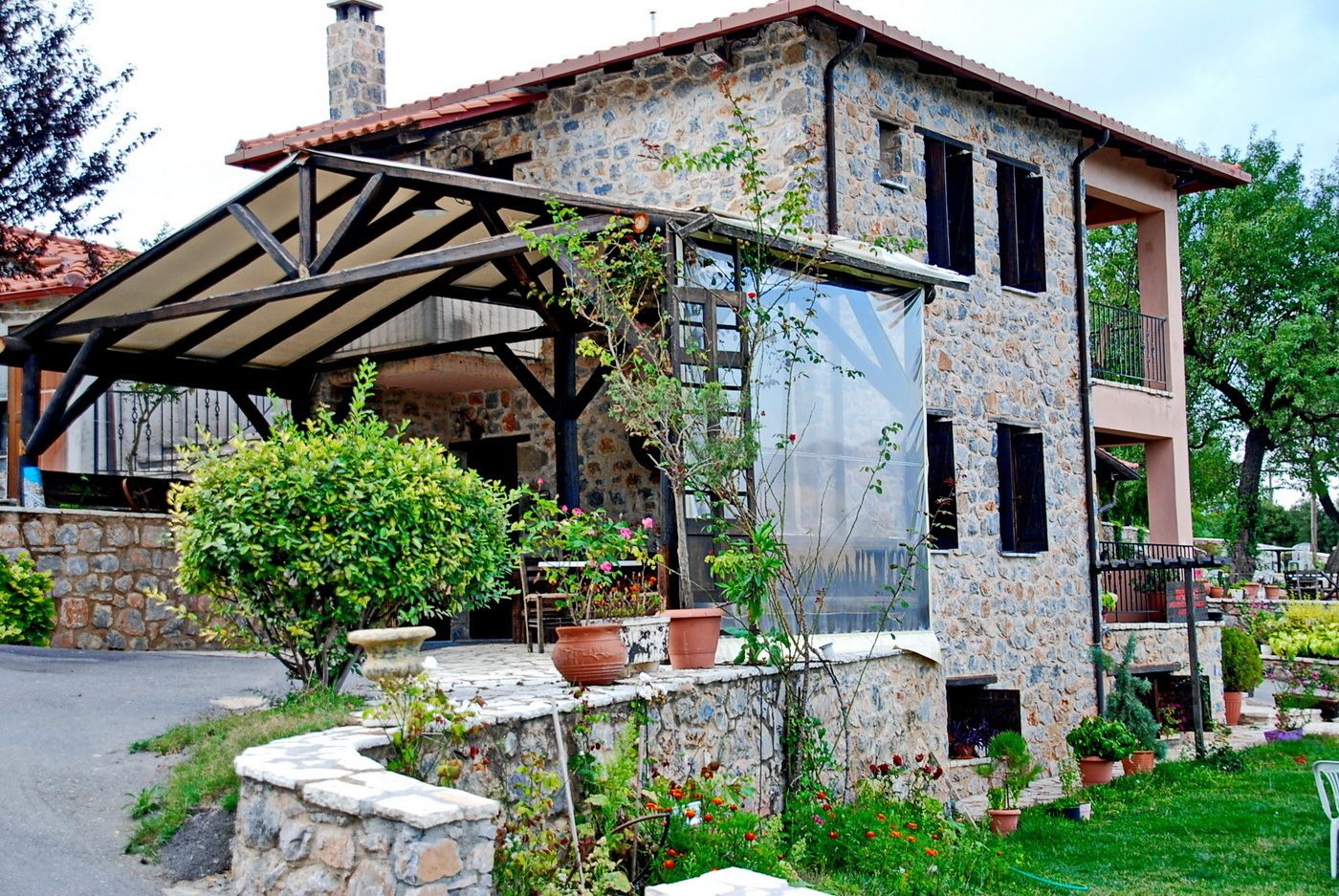 A stone building with a covered patio, potted plants, and a garden.