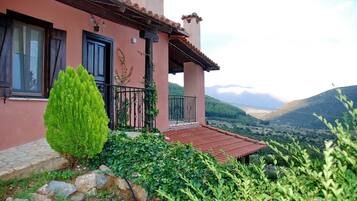 A house with a red-tiled roof, a balcony with a black railing, and a view of a valley with mountains in the background.
