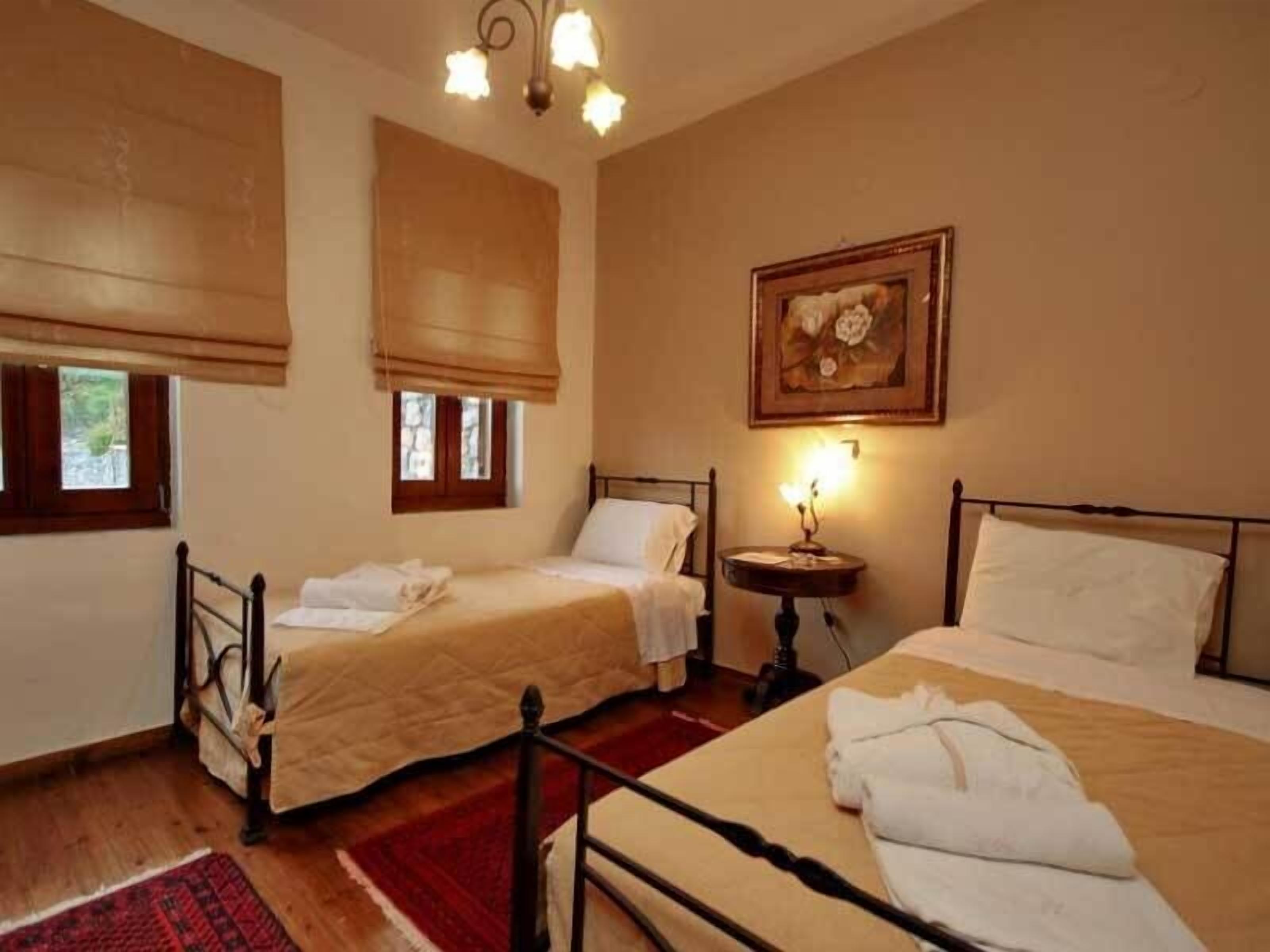 A hotel room with two beds, a chandelier, a painting, and a window with blinds.