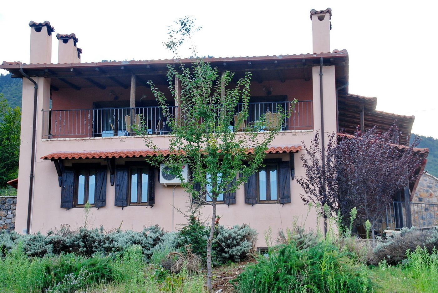 Un bâtiment à deux étages doté d’un balcon, d’un mur en pierre et d’un arbre au premier plan.