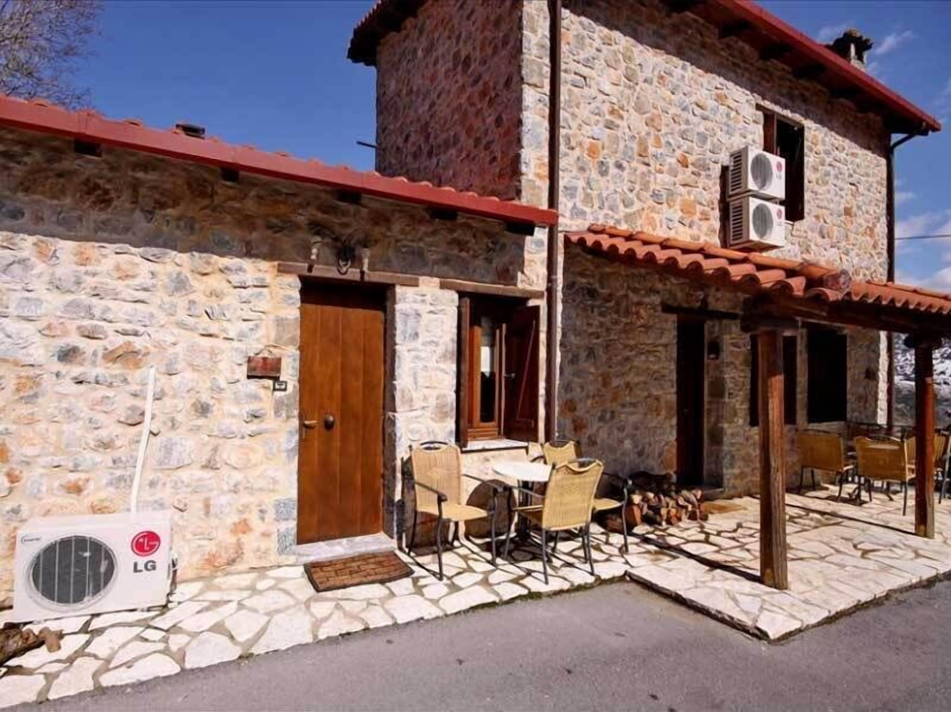 A stone building with a red roof, an outdoor seating area with chairs and tables, and an air conditioning unit labeled LG.