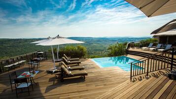 A wooden deck with a pool, lounge chairs, and umbrellas.