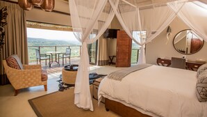 A bedroom with a large bed, a desk, a chair, and a balcony with a view. - Umzolozolo Private Safari Lodge (Ladysmith)