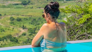 A person in a swimming pool with a view of a green landscape. - Umzolozolo Private Safari Lodge (Ladysmith)