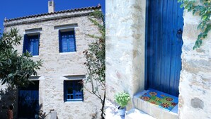 A stone building with blue doors and windows, a potted plant, and a colorful mat at the entrance. - Villa Sofas (Platanias)