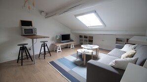 Quarto compacto e bem iluminado com beliche, escrivaninha com computador, televisão e sofá.