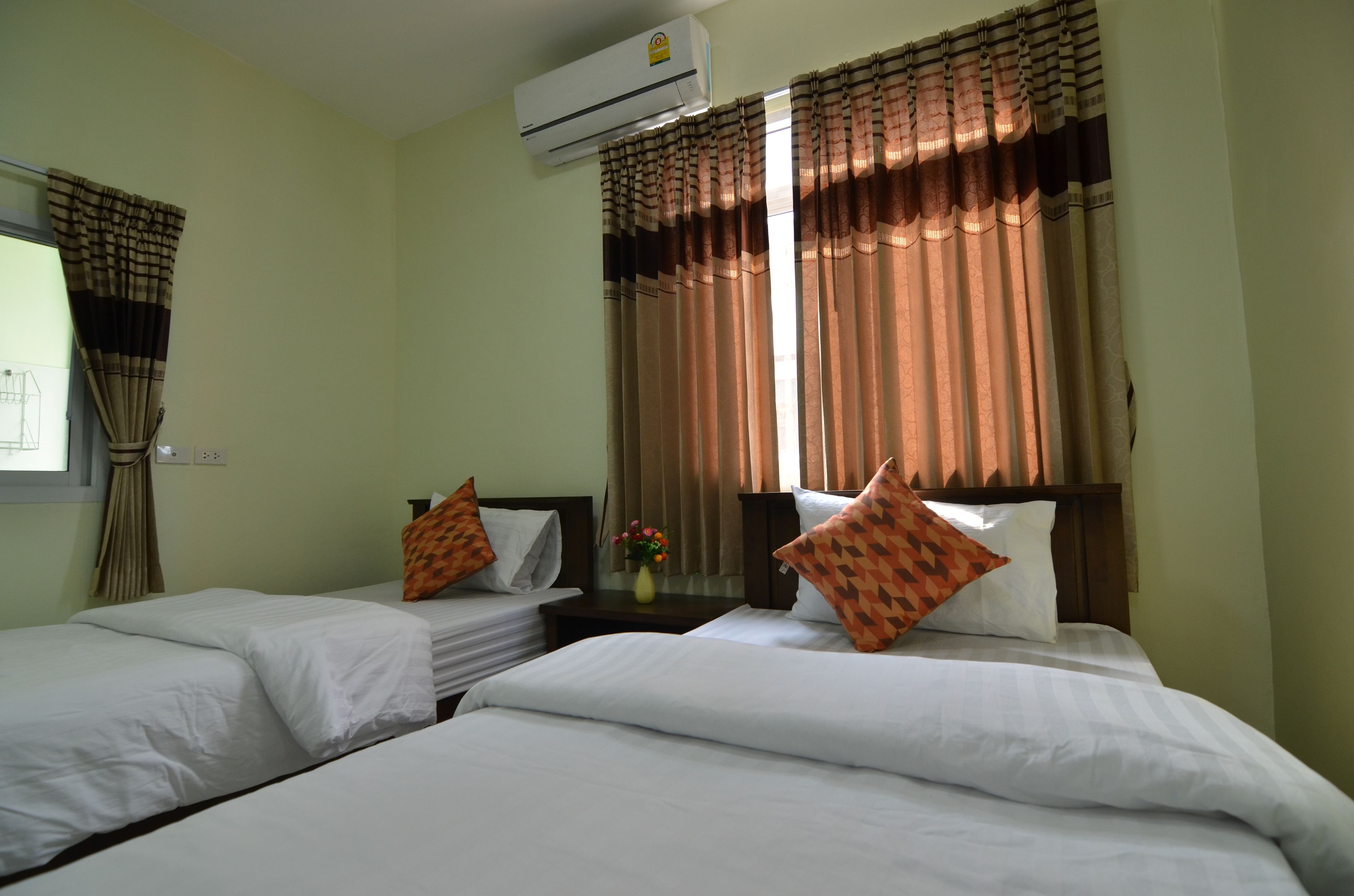 A hotel room with two single beds, a nightstand with a vase of flowers, and a window with curtains.