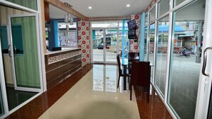 A hotel reception area with a glass door leading outside, a reception desk, and a seating area with chairs. - The Best Place (Samut Prakan)