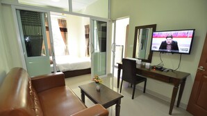 A hotel room with a sofa, a desk, a TV, and a bed with curtains. - The Best Place (Samut Prakan)