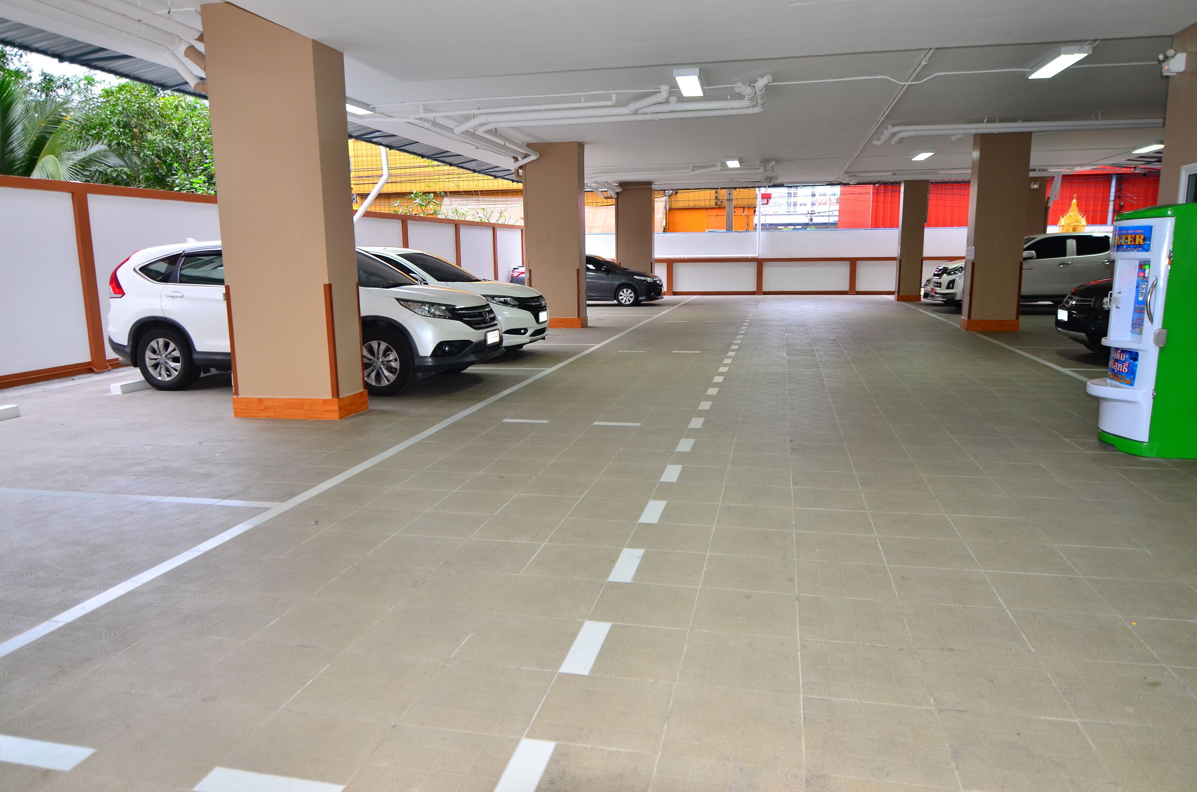 A parking garage with multiple cars parked, concrete pillars, and a vending machine.