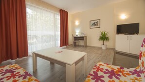 A furnished room with a desk, a television, a potted plant, and a window with curtains. - Mariner's Suites (Sunny Beach)