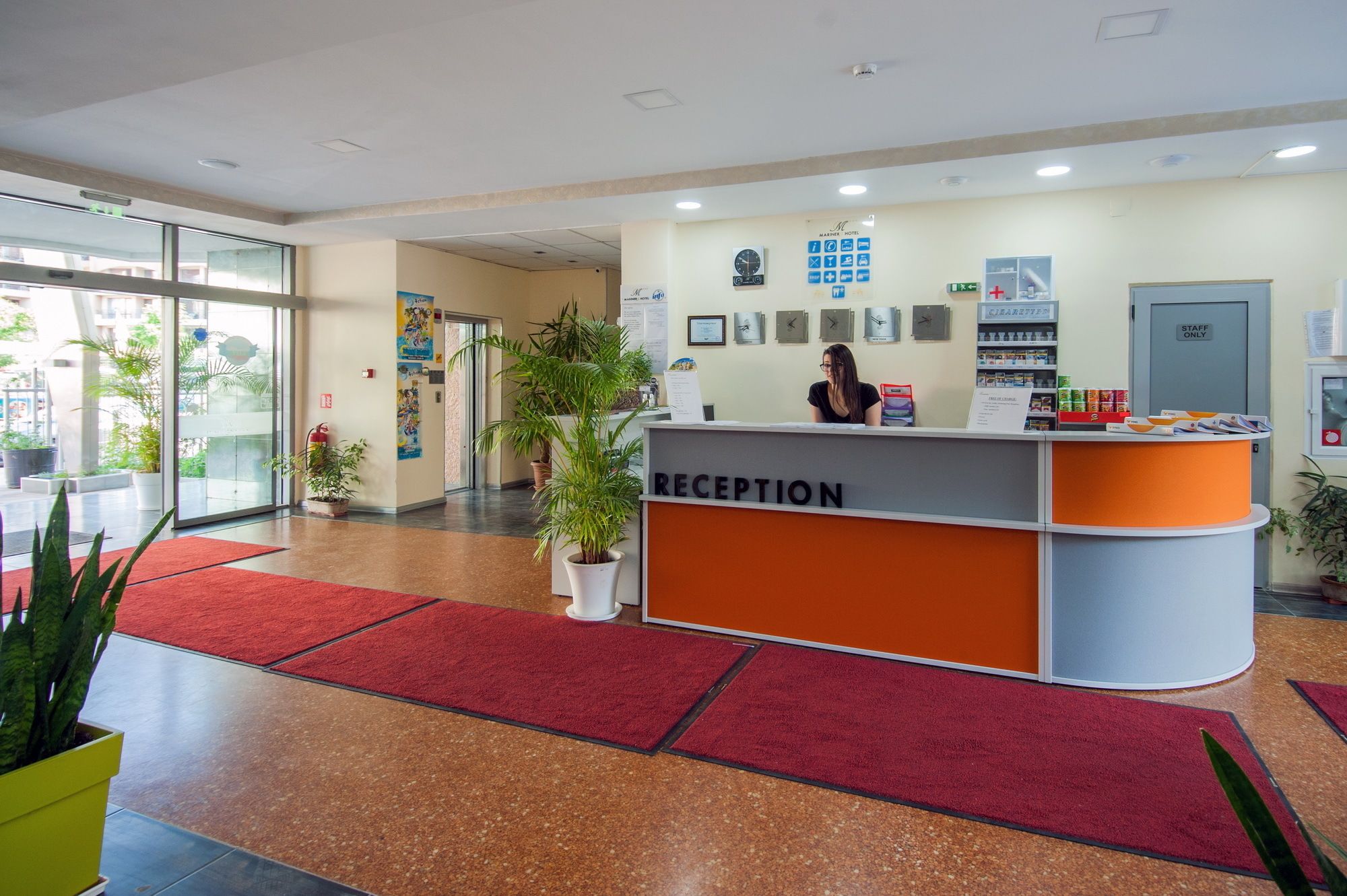 A reception area with a reception desk, potted plants, and a clock on the wall.