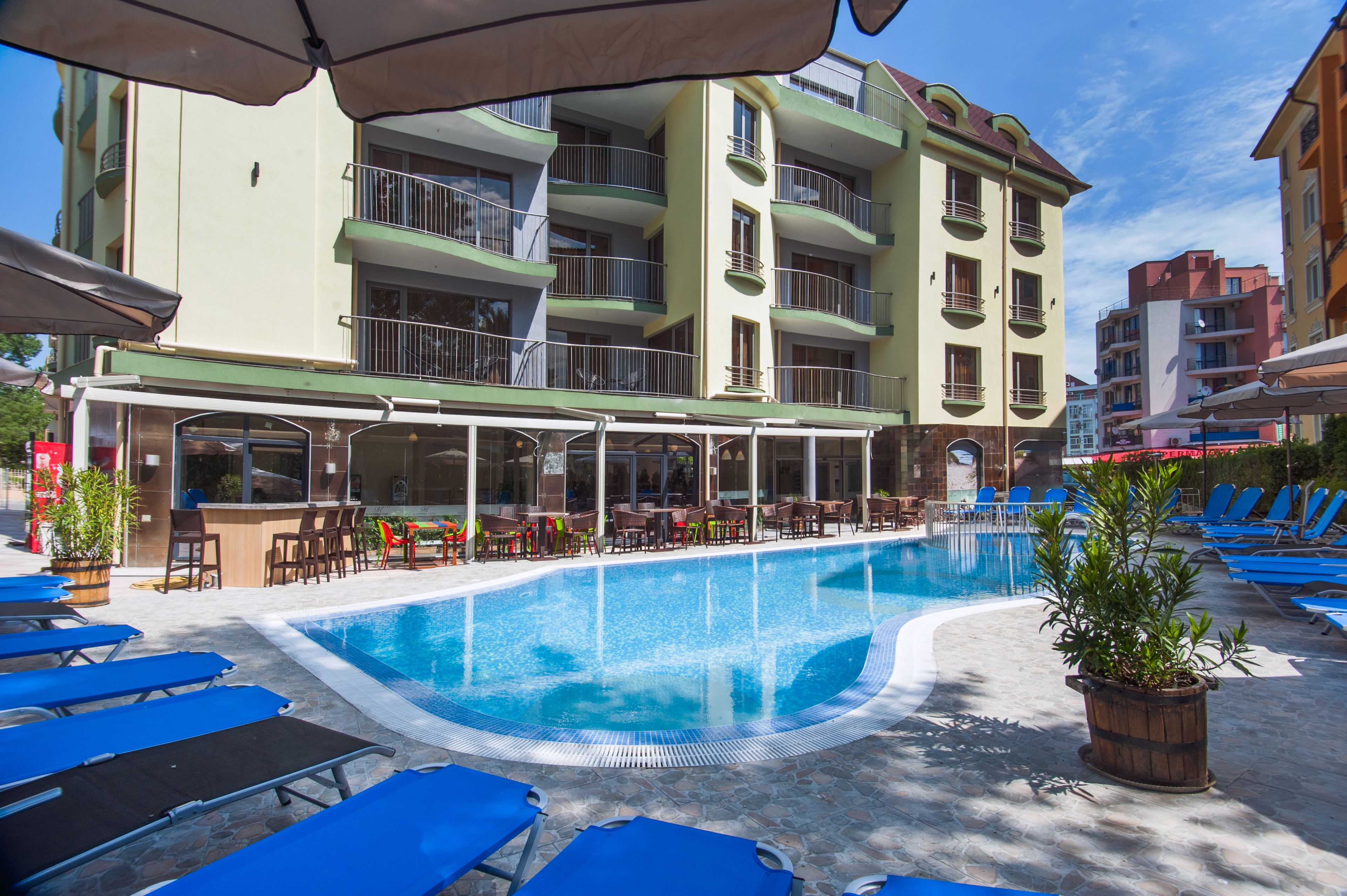 A swimming pool with lounge chairs and a bar area, surrounded by multi-story buildings with balconies.