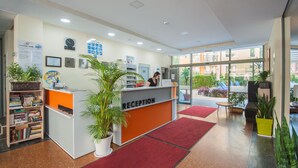 A reception area with a reception desk, a plant, a bookshelf, and a view of the outdoor seating area. - Mariner's Suites (Sunny Beach)