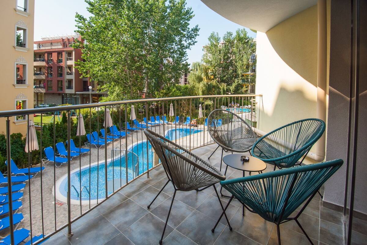 A balcony with a swimming pool, blue lounge chairs, and wicker chairs.