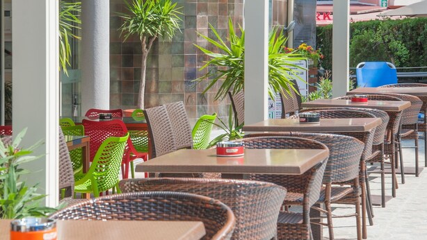 A row of wicker tables and chairs in an outdoor cafe setting. - Mariner's Suites (Sunny Beach)