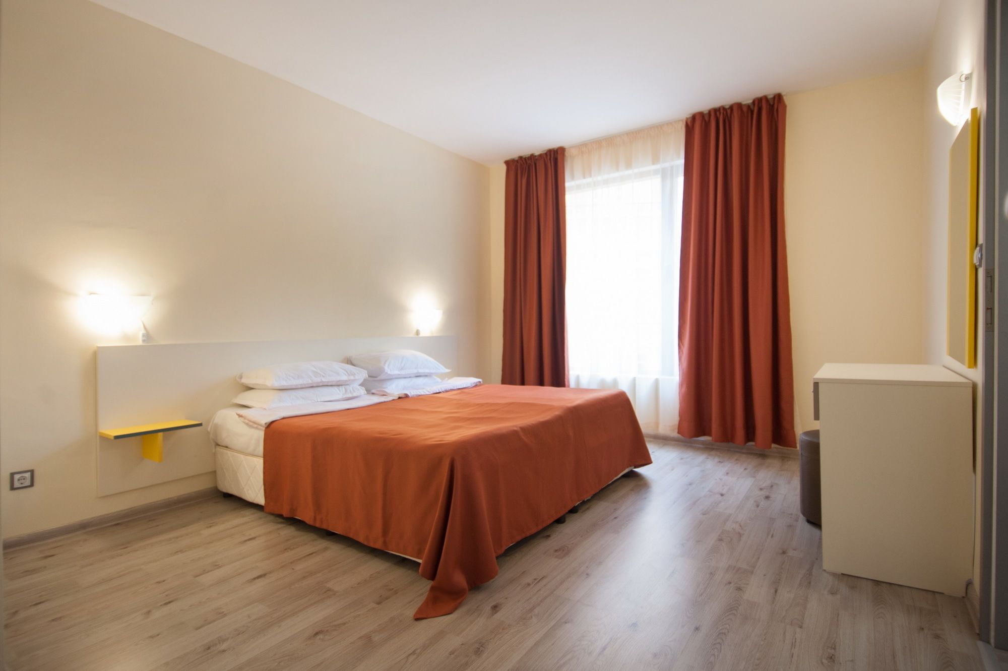A bedroom with a bed, bedside lamps, a small table, and a window with curtains.