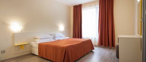 A bedroom with a bed, bedside lamps, a small table, and a window with curtains.