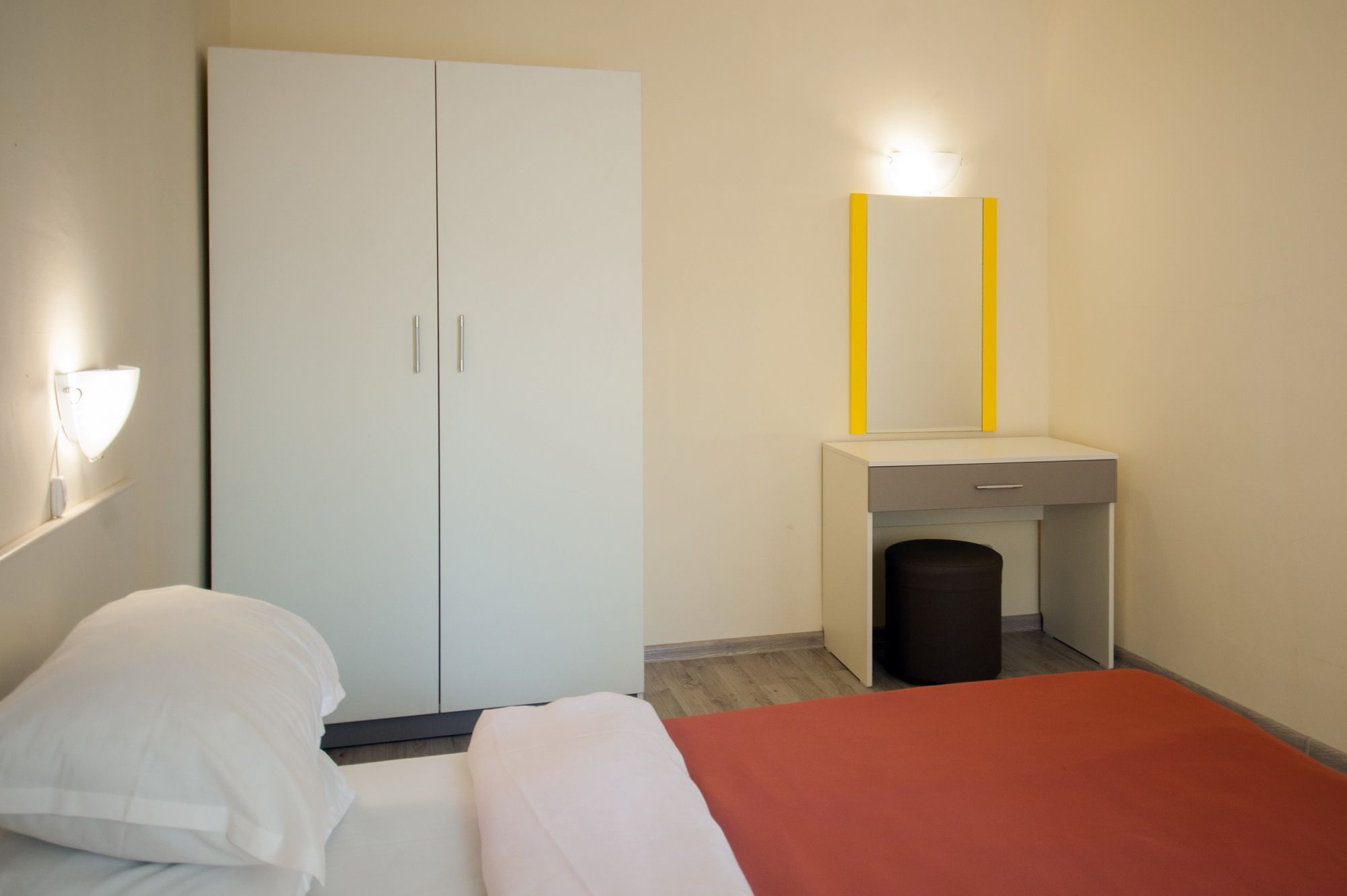 A bedroom with a bed, a wardrobe, a bedside table, a mirror, and a wall-mounted light.