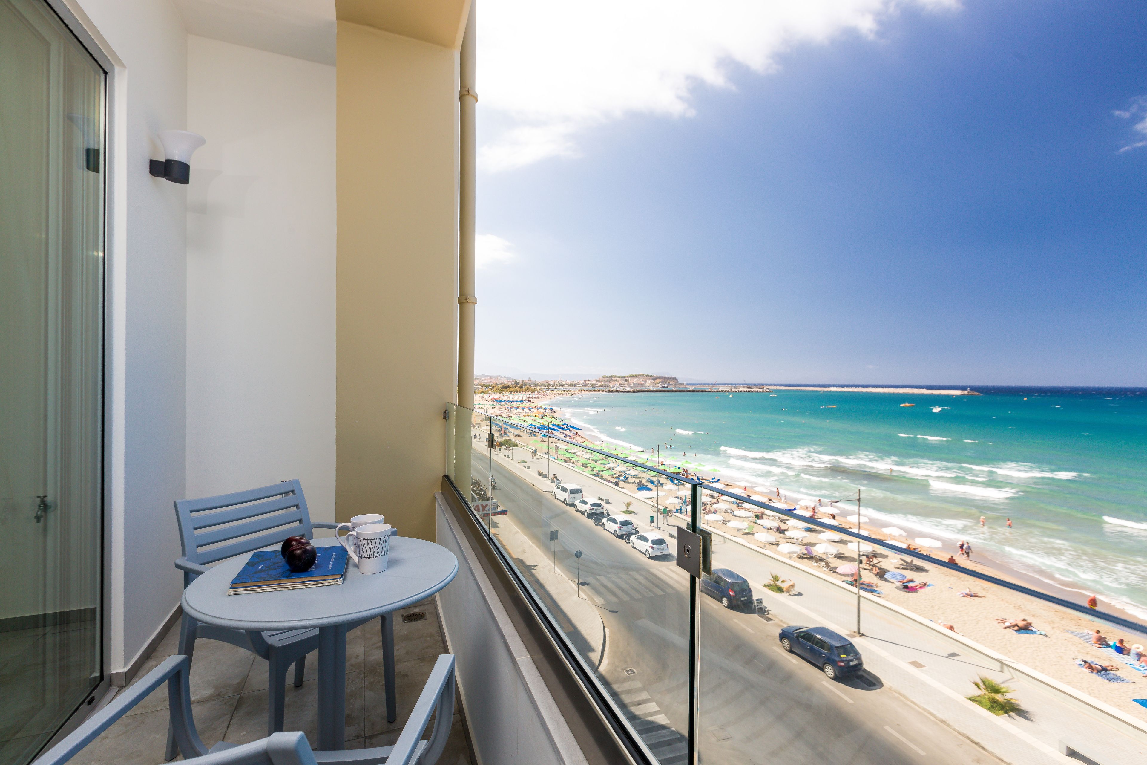 A balcony with a view of a beach, a table with a book and a mug, and a chair.
