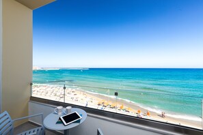 A balcony with a view of a beach, a table with a tablet and a mug, and a chair. - Meltemi Coast Suites (Rethymno)